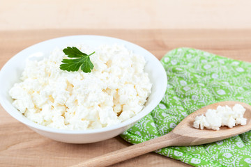 Fresh cottage cheese in a white bowl with spoon on a wooden.