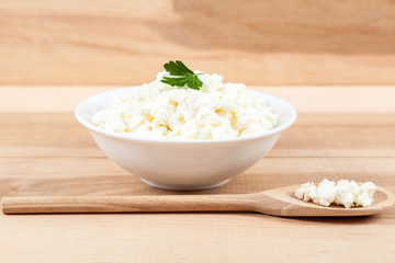 Fresh cottage cheese in a white bowl with spoon on a wooden.