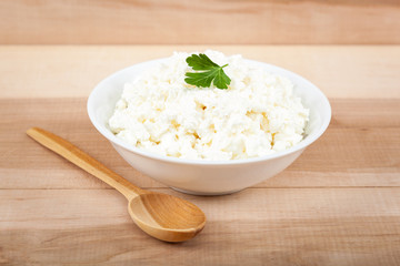 Fresh cottage cheese in a white bowl with spoon on a wooden.