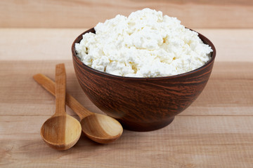 Fresh cottage cheese in a bowl with spoon on a wooden.