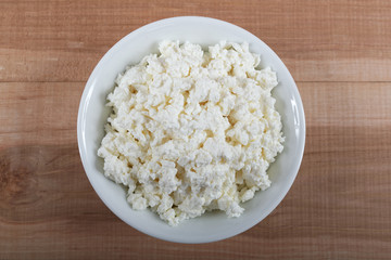 Fresh cottage cheese in a white bowl on a wooden.