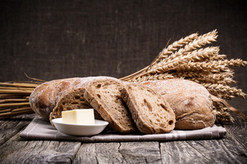 Tasty bread with wheat on wooden background.