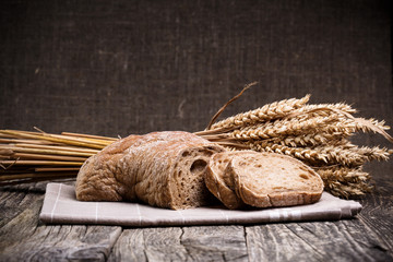 Tasty bread with wheat on wooden background.