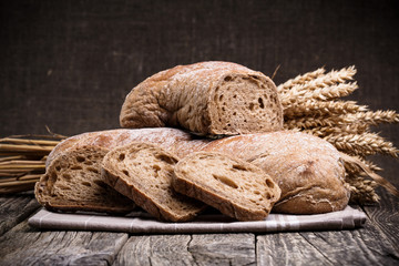 Tasty bread with wheat on wooden background.