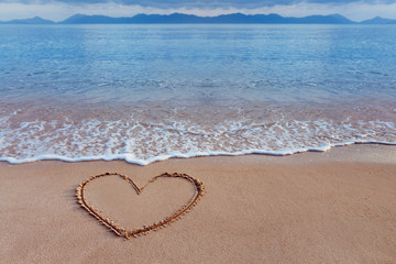A drawing of a heart as a love symbol on a yellow sand at a seas