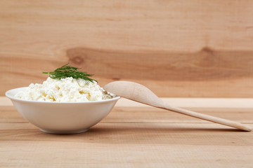 Fresh cottage cheese in a white bowl with spoon on a wooden boar
