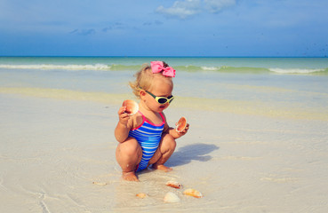 cute little girl playing with shells on the beach