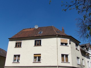 Pastellfarbenes Eckhaus in Beige und Naturfarben mit alten Rollläden vor blauem Himmel im...