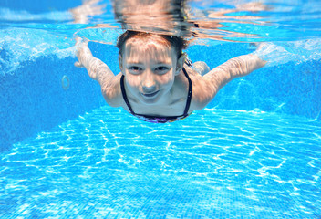 Fototapeta premium Szczęśliwa dziewczyna pływa w basenie pod wodą, aktywne dziecko pływanie