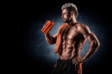 Young adult man drinking protein shake in gym. Black background.