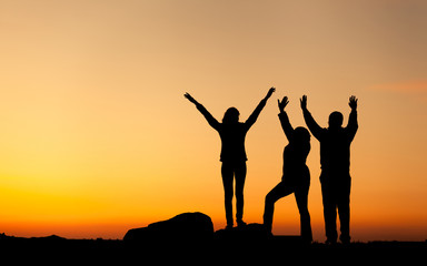 Silhouette of a happy family with arms raised up at the sunset