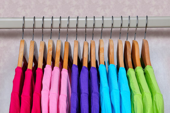 Multicolored women's t-shirts hanging on wooden hangers.