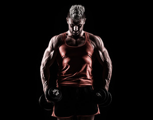 Closeup of a muscular young man lifting weights on dark backgrou