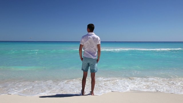 Young man standing on beach with hands in pockets
