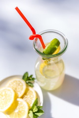 Lemonade in the jug with red straw and lemons on plate
