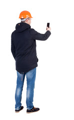 Backview of an engineer in construction helmet stands and using