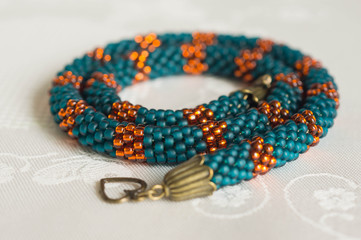 Knitted necklace from beads of emerald and orange color