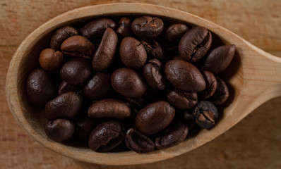 whole coffee beans in spoon on wooden background