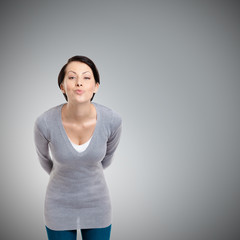 Obraz premium Beautiful lady throws a kiss and hides hands behind the back, isolated on grey