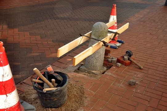 Eine kleine Baustelle mit Sicherheitsh&uuml;tchen, Betonpfeiler und Stra&szlig;ensch&auml;den ausbessern