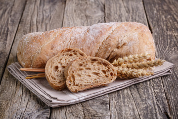 Tasty bread with wheat on wooden background.