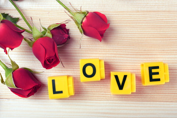 Beautiful roses with word LOVE on wooden background