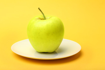 Apple on saucer on color background