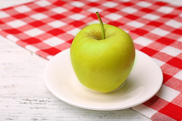 Apple on saucer with napkin on wooden table, closeup