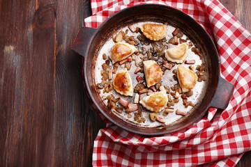 Fried dumplings with onion and bacon in frying pan,