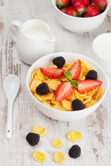 cornflakes with berries in a bowl and milk for breakfast, close-