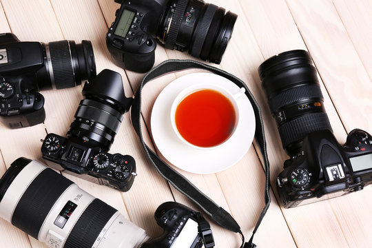 Modern cameras with cup of tea  on wooden table, closeup