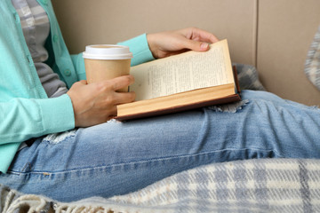 Young woman reading book, close-up, on home interior background