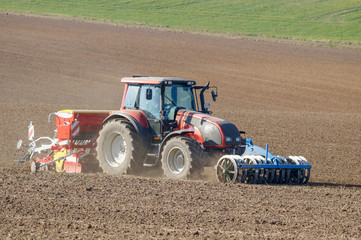 Obraz premium Frühjahrsbestellung, Schlepper mit Sämaschine, Hügellandschaft