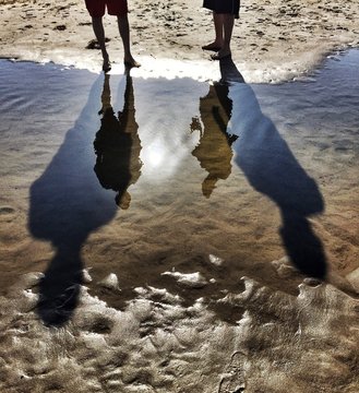 Reflections And Tall Shadows Of Two People At The Beach