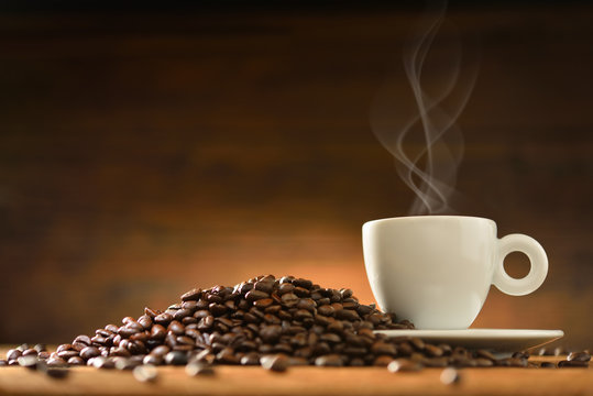 Cup of coffee with smoke and coffee beans on wooden background © amenic181