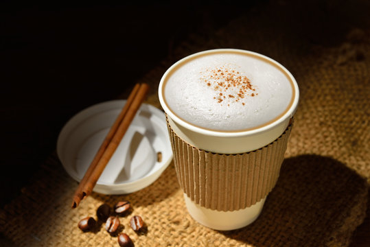 Paper cup of coffee and coffee beans on wooden table