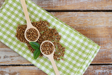 Coriander seeds on wooden spoons on checkered cloth