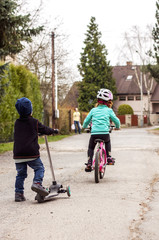 A boy on  a scooter and a girl riding home from a shop.