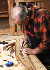 Senior carpenter restoring old furniture with chisel in his workshop.