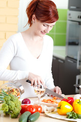 Smiling young woman cutting vegetables in kitchen.