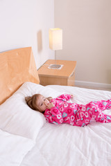 Small girl in pink pajamas lying resting on a bed