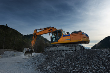 sideview of huge orange shovel excavator digging in gravel