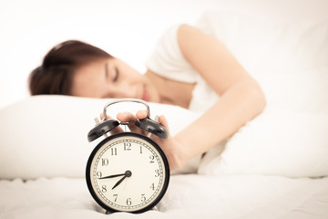 Woman in bed trying to wake up with alarm clock