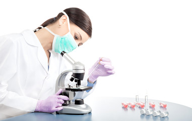 Woman in face mask uses pipette and microscope.