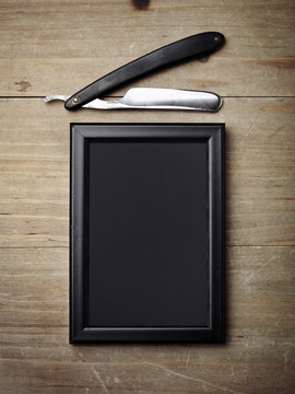 Straight razor and black picture frame on wood desk