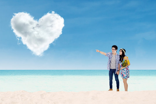 Couple with heart shaped cloud at beach