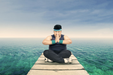 Overweight man meditating on the jetty 1