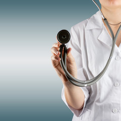 Female doctor's hand holding stethoscope on blurred background.