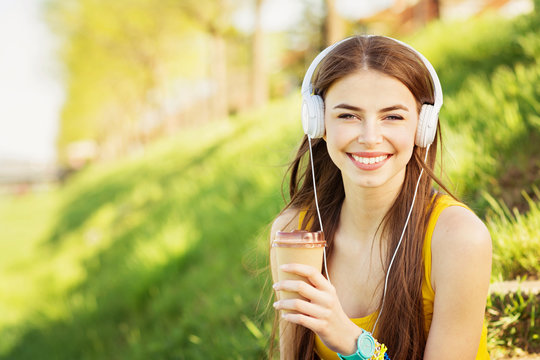 Happy teenage girl with headphones and takeaway coffee