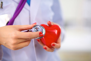 Doctor with stethoscope examining red heart, isolated on white